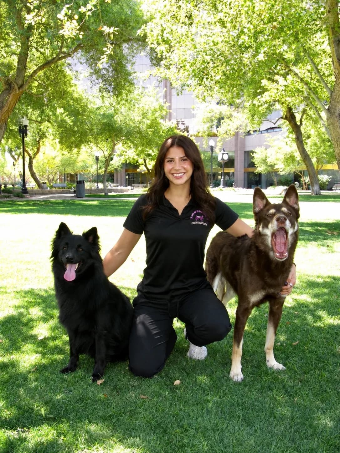 Sam’s Happy Tails trainer kneeling between two dogs in a park
